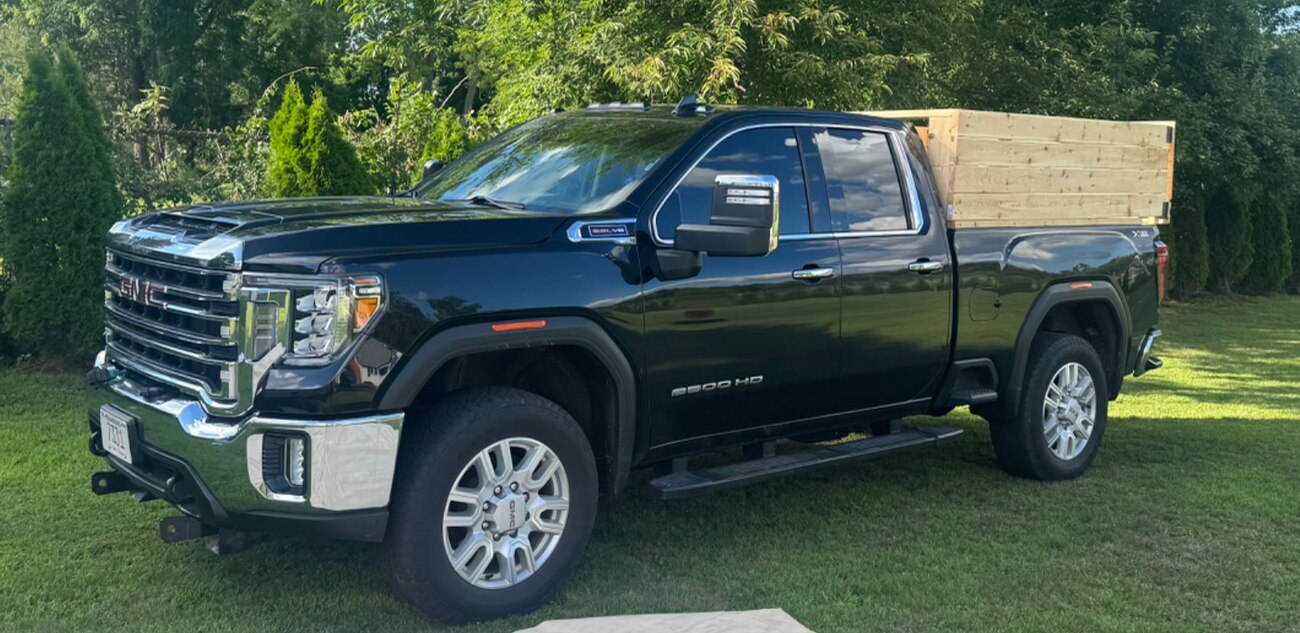 Close view of the Colonial Cleanouts black GMC 2500HD pickup with chrome grille, tow mirrors, and wooden bed sides